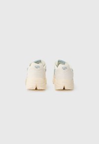 Light cream athletic shoes with a smooth texture, featuring a teal accent on the heel, and a durable Vibram sole for traction.