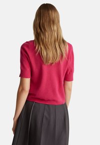 Fuchsia Kurzarmpullover aus weichem Strickmaterial, mit rundem Halsausschnitt und geripptem Saum, kombiniert mit einem dunklen Faltenrock.