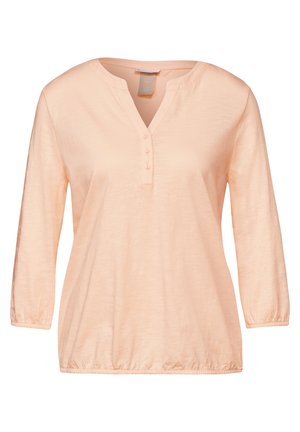 Haut long à manches en pêche clair avec un décolleté en V, doté d'une patte de boutonnage et de poignets froncés, fabriqué à partir d'un tissu doux et léger.