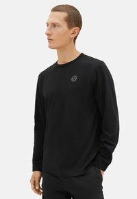 Zwarte langslieve T-shirt gemaakt van zacht materiaal. Bevat een ronde hals en een klein logo op de linkerborst. Rechte snit met minimale accenten.