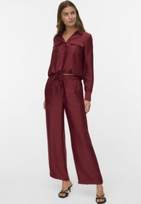 Burgunderfarbene Satin-Zweiteiler-Set bestehend aus einem knöpfbaren Hemd mit zwei Brusttaschen und einer weiten Hose mit elastischem Bund.