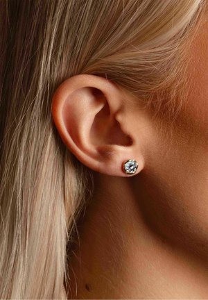 Gold stud earrings featuring a clear round gemstone centerpiece, set against the ear, with smooth texture and polished finish.