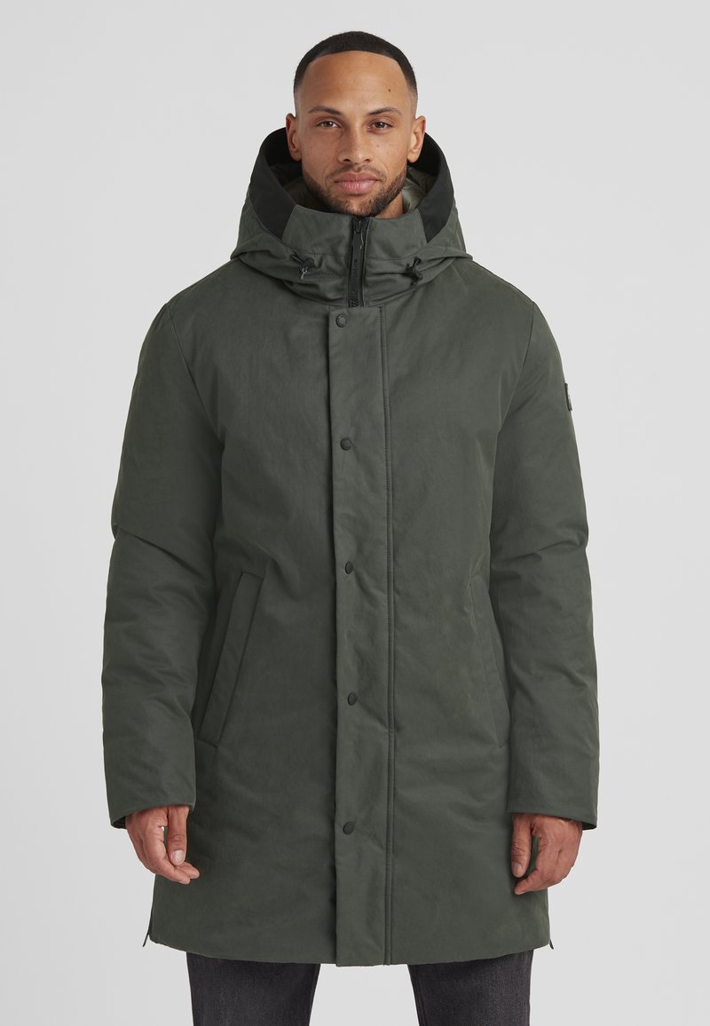 Dunkelgrüne Parka-Jacke mit Kapuze, versehen mit einem Reißverschluss und Knopfverschluss, seitlichen Taschen und einem strukturierten Stoff. Design in Mid-Thigh-Länge.