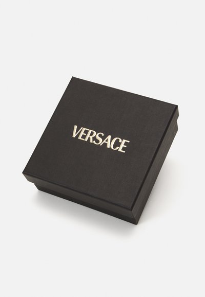 Čierna textúrovaná krabička so zlatým logom "VERSACE" na vrchu, s štvorcovým dizajnom a hladkým povrchom. Vhodná na šperky alebo doplnky.