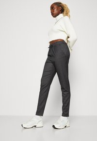 Pantalons noirs à rayures avec une taille à cordon, associés à un col roulé blanc à côtes et des chaussures de sport blanches.