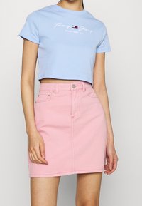 Light blue cropped t-shirt with 'Tommy Jeans' logo and pink denim skirt featuring front pockets and a button closure. Soft cotton blend.