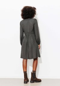 Robe gris foncé à manches longues, taille élastique et petits points dispersés. Associée à des bottines marron à côtés élastiques.