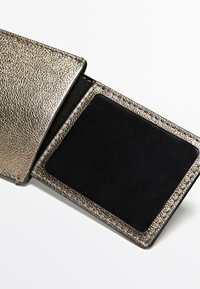 Metalická bronzová peněženka s texturovaným povrchem a černým vnitřkem. Vnitřek obsahuje hladkou černou část na držení karet.