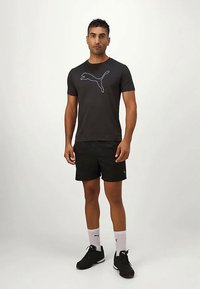 Čierne tričko s krátkym rukávom s bielym logom Puma, kombinované s čiernymi šortkami, bielymi ponožkami a čiernymi športovými topánkami. Jednoduchý, športový dizajn.