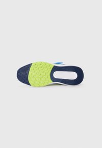 La semelle de la chaussure présente un motif de texture, principalement noir et vert, avec une semelle intermédiaire blanche et des accents bleus près du talon.
