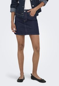 Temno jeans krilo do stegen s ravnim krojem, kontrastnim šivom in sprednjimi žepi, v kombinaciji s črnimi balerinkami in jeans jakno.