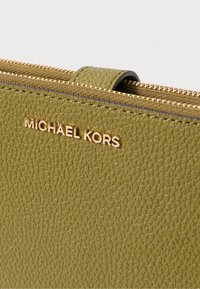 Olijfgroene leren portefeuille met een gestructureerd oppervlak, gouden "MICHAEL KORS" logo en gouden ritssluiting langs de bovenrand.