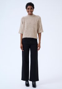 Beige fluffy knit sweater with short sleeves, paired with high-waisted black wide-leg jeans and black ankle boots. Simple, textured outfit.