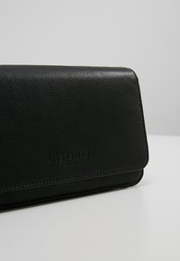 Czarna skórzana kopertówka o fakturowanej powierzchni i zamknięciu na klapę. Zdobiona tłoczonym logo. Czysty, prostokątny kształt o minimalistycznym designie.