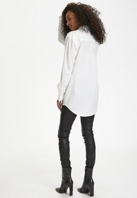 Witte blouse met lange mouwen en een afgeronde zoom, gecombineerd met gestructureerde zwarte leren leggings en enkellaarsjes met een blockhak.