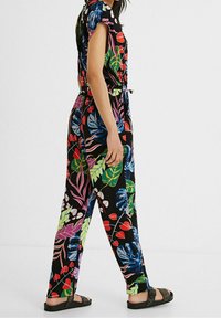 Blommig jumpsuit i svart tyg med färgglada blad och blommor, korta ärmar, elastisk midja och avsmalnande ben. Avslappnad passform med sandaler.