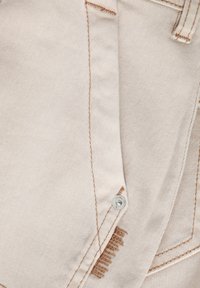 Bežna denim tkanina s kontrastnim bežnim šivanjem. Ima vidno kovinsko gumba in obrabljeno območje blizu šiva.
