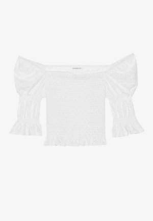Haut blanc décolleté avec des manches bouffantes, corsage froncé et ourlet à volants évasés. Fabriqué en coton texturé avec des détails en broderie anglaise.