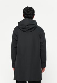 Pikk must jope kapuutsiga, valmistatud siledast ja kergest materjalist. Omab sirget lõiget ja pikki varrukaid, õlgadel on nähtavad õmblused.