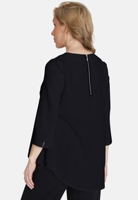 Blusa nera con maniche a tre quarti, dotata di scollo rotondo e zip verticale sul retro. Texture morbida e liscia con una vestibilità fluida.