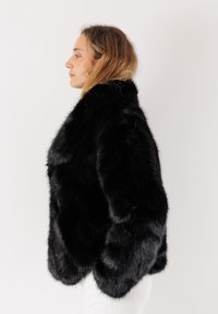 Giacca in pelliccia sintetica nera con una texture morbida, vestibilità rilassata e ampio colletto. Caratterizzata da maniche lunghe e orlo arrotondato.