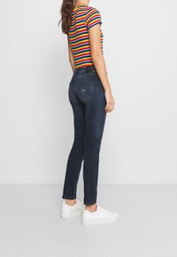 Mörkblå jeans med slim fit och klassisk femficksdesign, kombinerat med en flerfärgadrandig t-shirt med kort ärm och vita sneakers.
