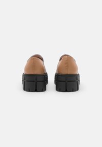 Chaussures en cuir marron avec une semelle chunky noire, présentant une texture lisse et un design à dos arrondi. Aucun élément décoratif visible.