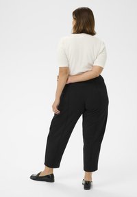Pantaloni negri tapered cu o textură fină, asortați cu un top de culoare deschisă cu mânecă scurtă. Încălțările sunt loferi negri.
