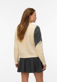 Kreemikas-hall triibuline kootud kampsun pärlmuttermustriga varrukatel, kombineeritud volditud tumeda halli seelikuga.