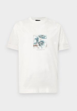 Vit bomulls-T-shirt med ett tryck framtill som visar abstrakta blå och bruna mönster samt texten "EMPORIO ARMANI" under bilden.