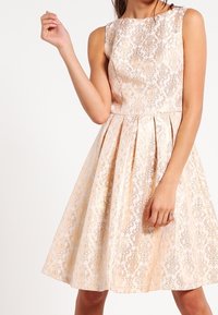 Bezramenné šaty do kolen v bledě zlaté barvě s ozdobným květinovým vzorem, s upnutým korzetem a rozšířenou sukní.