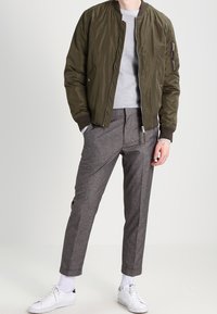 Kurtka bomberka w kolorze oliwkowej zieleni z kieszeniami na zamek, jasnoszary sweter o fakturze, szare spodnie w kratę oraz białe trampki.