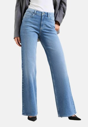 Light blue wide-leg jeans made of denim, featuring a high waist, front pockets, and a clean hem. Worn with a fitted white top and black shoes.