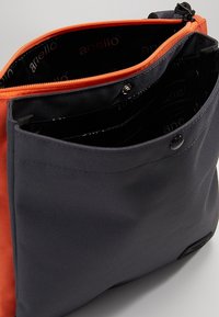 Stylová černá a oranžová taška se hladkým povrchem, s oranžovým zipem a několika vnitřními kapsami pro organizaci.