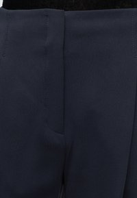 Gros plan de la ceinture d’un pantalon bleu marine avec des coutures visibles et une fermeture éclair.