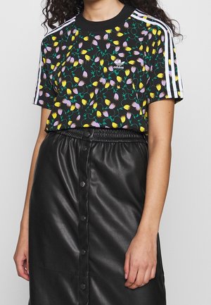 Sort t-shirt med blomsterdesign i gult og lilla, parret med en sort kunstlædernederdel med trykknapper.
