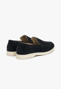 Zwarte suede instappers met een laag profiel, voorzien van crèmekleurige rubberen zolen en gestikte details op het bovenwerk.