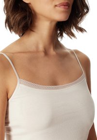 Light beige camisole with thin straps and a lace trim along the neckline. Smooth fabric texture, fitted design, and minimal coverage.