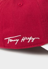 Rød baseballcaps laget av bomull, med en hvit brodert "Tommy Hilfiger"-logo på fronten. Capsen har en strukturert design og en buet brem.