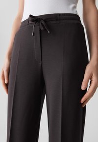 Pantaloni larghi grigio scuro realizzati in tessuto morbido, con vita regolabile, tasche laterali e una sottile trama a righe.