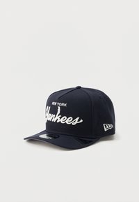 Casquette bleu marine en tissu structuré, avec "NEW YORK" et "Yankees" brodés en blanc. Visière courbée et logo sur le côté.