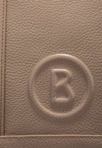 Matériau en cuir beige avec une surface texturée, présentant un logo circulaire en relief avec un "B" stylisé au centre.