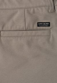 Pantalon beige pour homme avec une poche arrière et une étiquette noire cousue au-dessus de la poche indiquant « STREET ONE MEN Unmatched Comfort ».