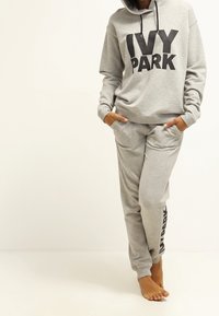 Szary zestaw z bluzy z kapturem i spodni dresowych z wyraźnym napisem "IVY PARK" w czarnym kolorze. Wykonany z miękkiego materiału, o luźnym kroju i z kieszeniami z przodu.