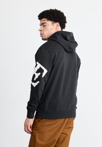 Μαύρο φούτερ με κουκούλα και λευκό γραφικό λογότυπο στην αριστερή μανσέτα. Κατασκευασμένο από μαλακό υλικό, διαθέτει ραμμένες μανσέτες και στρίφωμα.