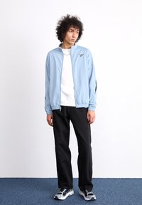 Light blue zip-up sports jacket with black accents, paired with a white T-shirt, black pants, and gray sneakers with blue details.
