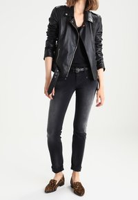 Svart läderbikerjacka med dragkedja fram, kombinerad med mörka jeans och bruna flats i leopardmönster. Slät textur och skräddarsydd passform.