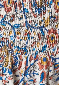 Telar con estampado floral en tonos azul, rojo y amarillo. La textura se reúne con fruncidos, sobre un fondo claro y neutro.