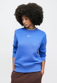 Μπλε φούτερ Nike με στρογγυλή λαιμόκοψη, ριμπ μανσέτες και τελείωμα. Διαθέτει μικρό λευκό λογότυπο στο στήθος. Λεία υφή υφάσματος.