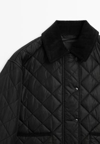 Zwarte doorgestikte jas met een corduroy kraag, drukknopen en twee voorzakken met een gladde textuur en ruitpatroon.